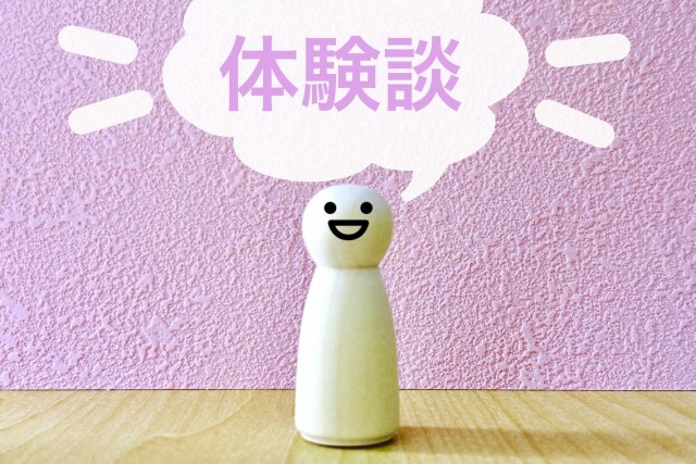 白い人型のオブジェが笑顔で立っており、背景に「体験談」と書かれたピンク色のボードが配置されているイメージ画像。