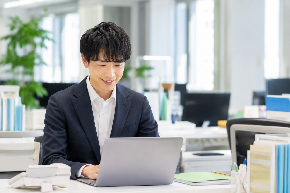 オフィスのデスクでノートパソコンに向かい前向きに働く会社員・就職後のイメージ