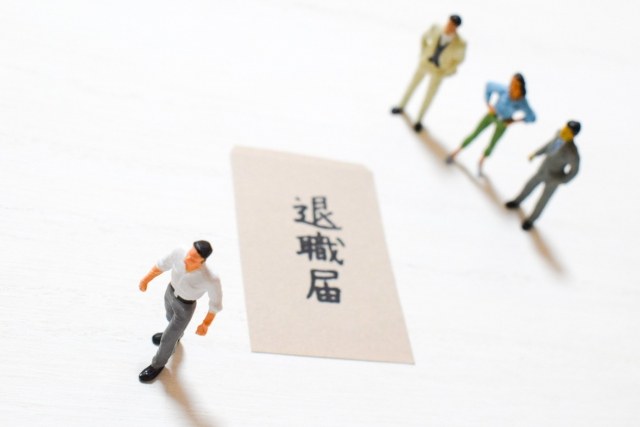 退職届の横を小さな人形が歩いているイメージ。退職の決断や新しい一歩を表現。