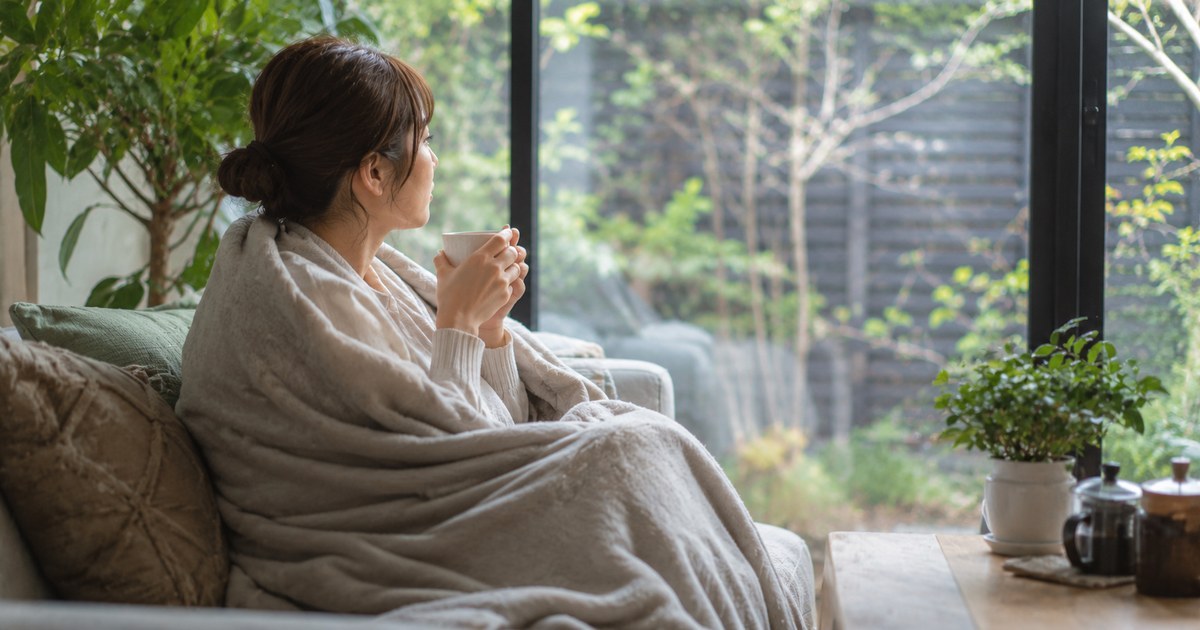 自宅でブランケットにくるまり温かい飲み物を手に休む様子