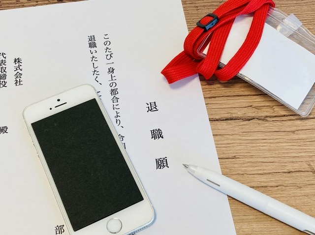 退職届とスマートフォン、赤いクリップが机に置かれている写真。退職手続きをイメージしたビジネスシーン。